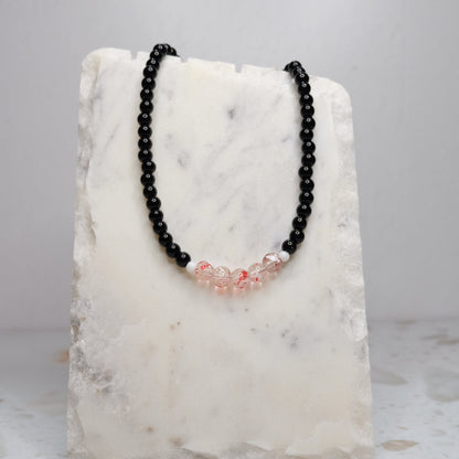 Black beaded necklace with red accents on a marble stand against a light gray background