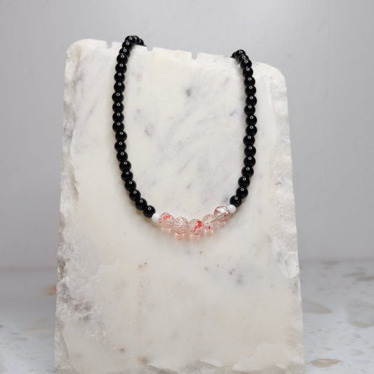 Black beaded necklace with red accents on a marble stand against a light gray background