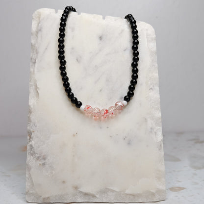 Black beaded necklace with red accents on a marble stand against a light gray background