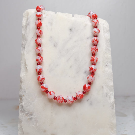 Necklace with red and white beads on a marble stand against a light gray background