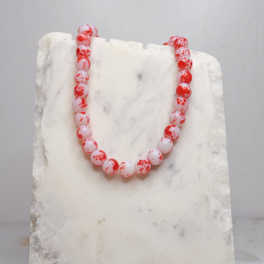 Red and white beaded necklace on a marble stand with a light gray background