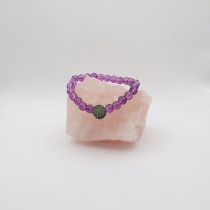 Purple beaded bracelet with a black  spiderweb bead  on a pink crystal against a white background