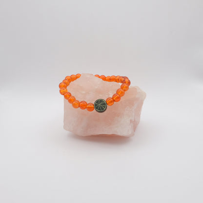 Orange beaded bracelet with a black  spiderweb bead on a pink stone against a white background