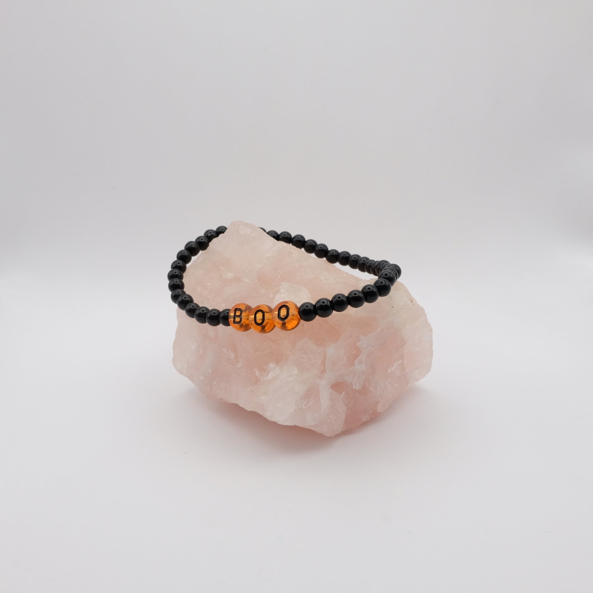 Black beaded bracelet with orange beads spelling 'BOO' on a pink crystal with a white background