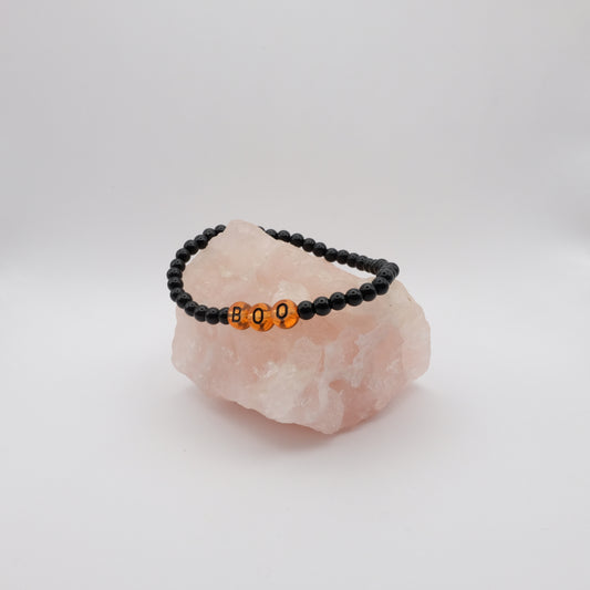 Black beaded bracelet with orange beads spelling 'BOO' on a pink crystal with a white background