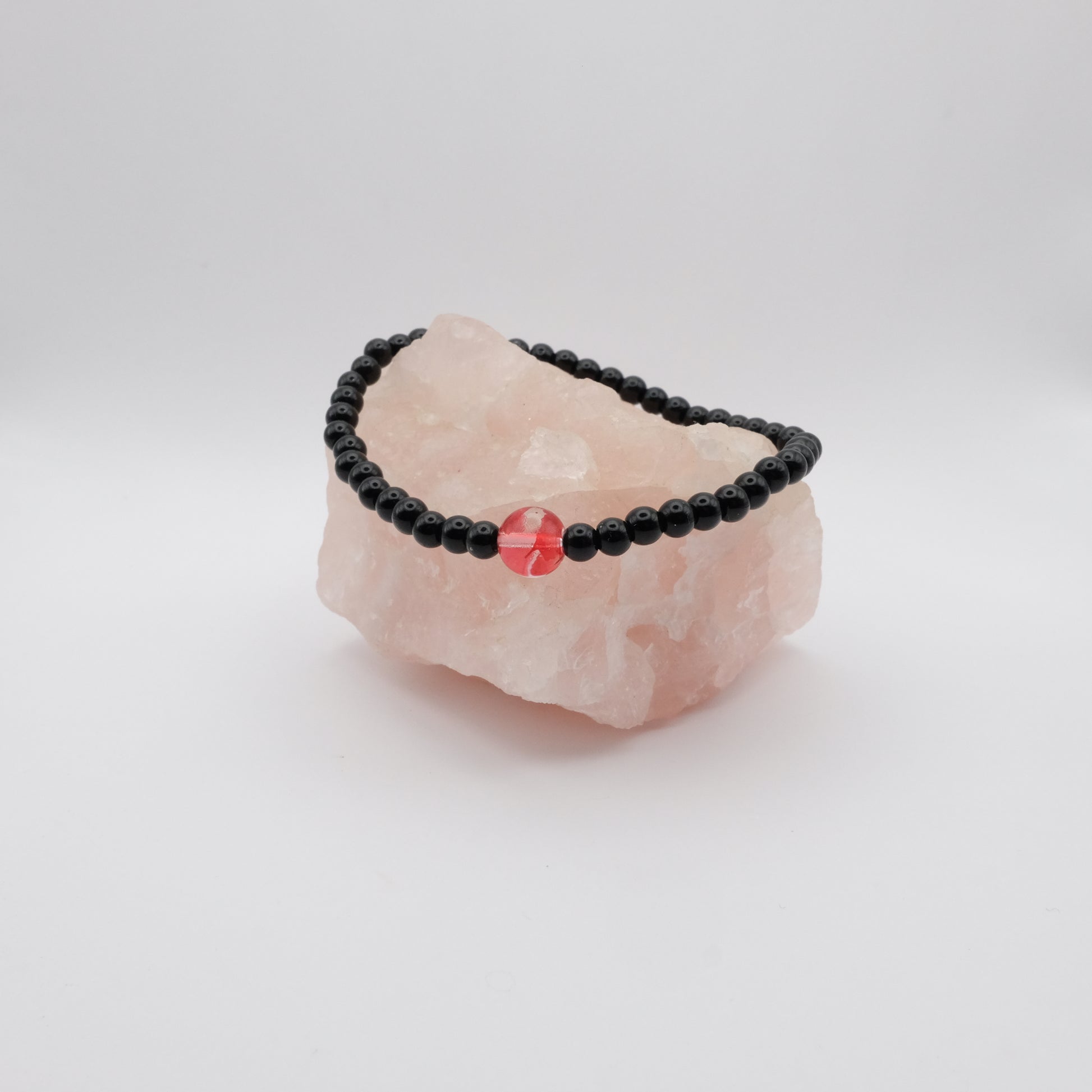 Black beaded bracelet with a red stone on a pink crystal
