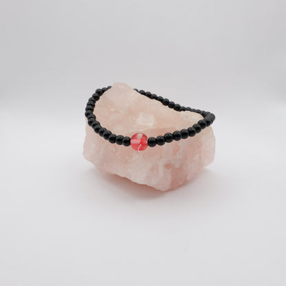 Black beaded bracelet with a red stone on a pink crystal