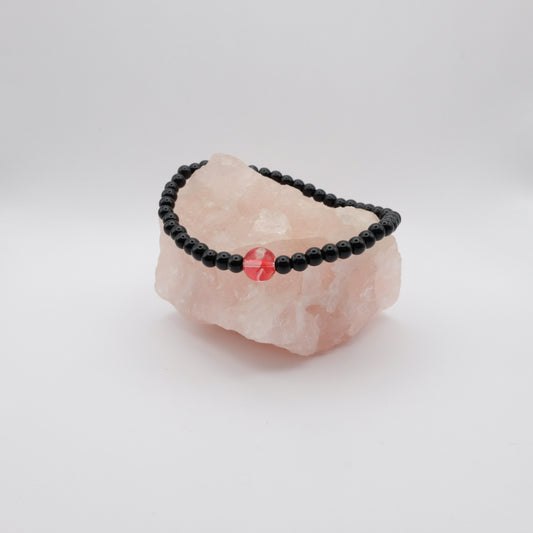 Black beaded bracelet with a red stone on a pink crystal