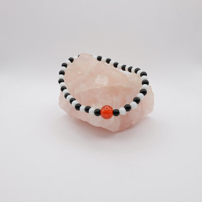 Beaded bracelet with black, white, and orange beads on a pink stone against a white background