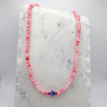 A beaded necklace composed of 6mm red and white marbled glass beads - featuring an 8mm blue and white marbled centre bead with small red accents, shown on a white marble background.