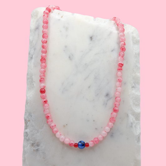 Necklace with red and white marble beads on a marble surface with a pink background