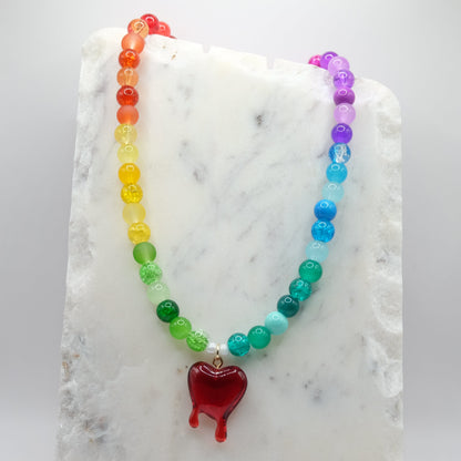 Rainbow glass beaded necklace with a red resin bleeding heart pendant on a marble surface.