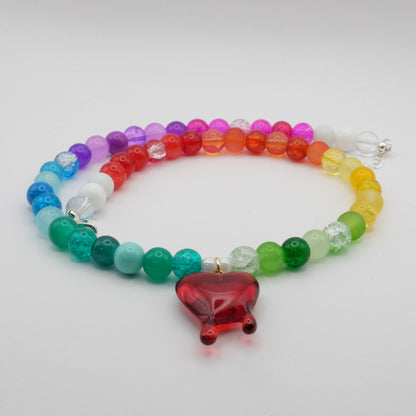 Rainbow beaded bracelet with a red resin bleeding heart charm on a light gray background