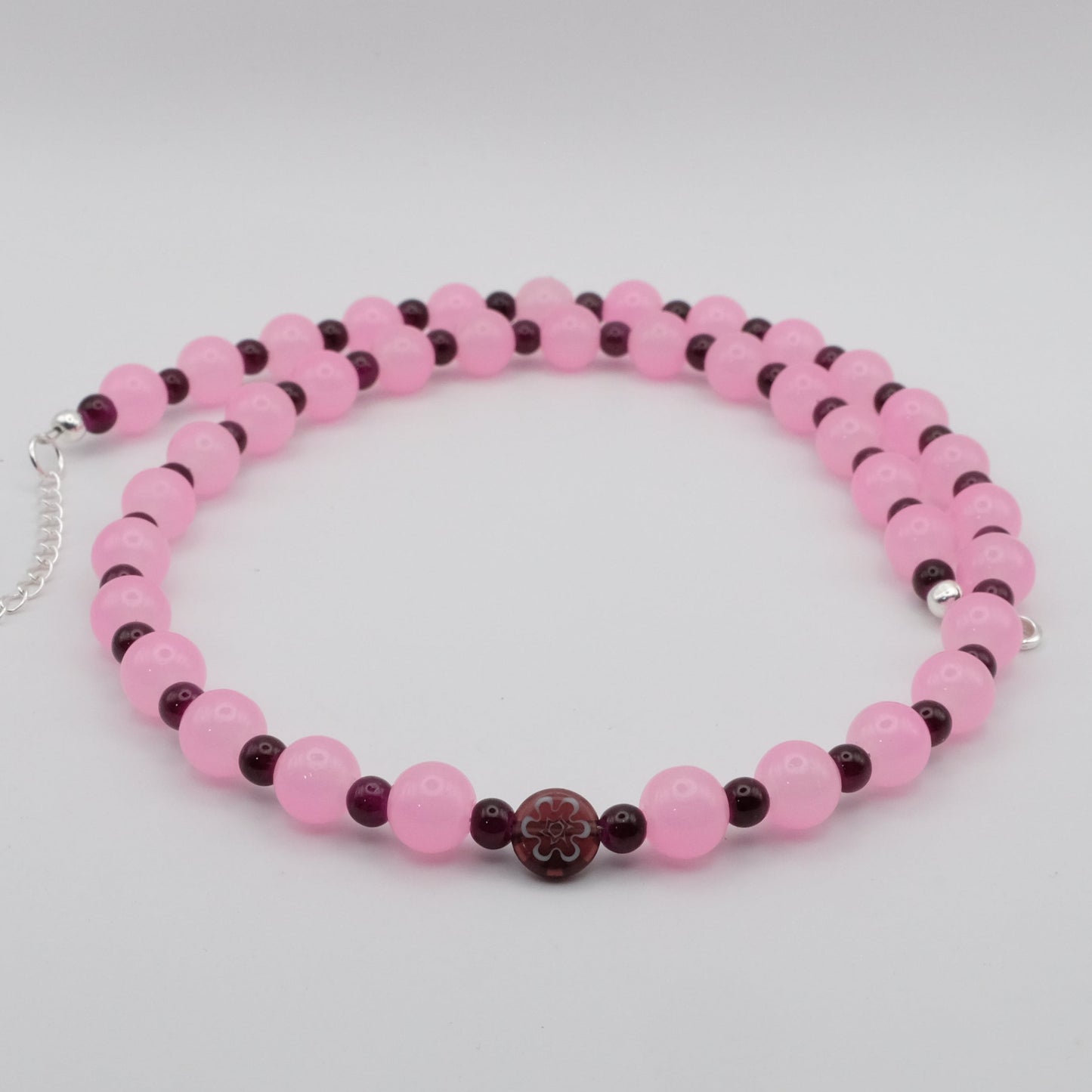 A handmade beaded necklace featuring alternating 8mm pink glass beads and 4mm deep plum glass beads with a flat glass flower focal bead, displayed on a white background.