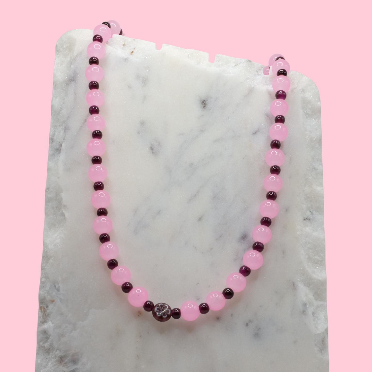 Beaded necklace with pink and purple beads on a marble surface with a pink background