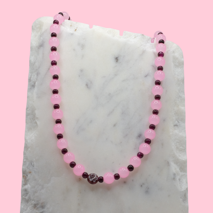 Beaded necklace with pink and purple beads on a marble surface with a pink background