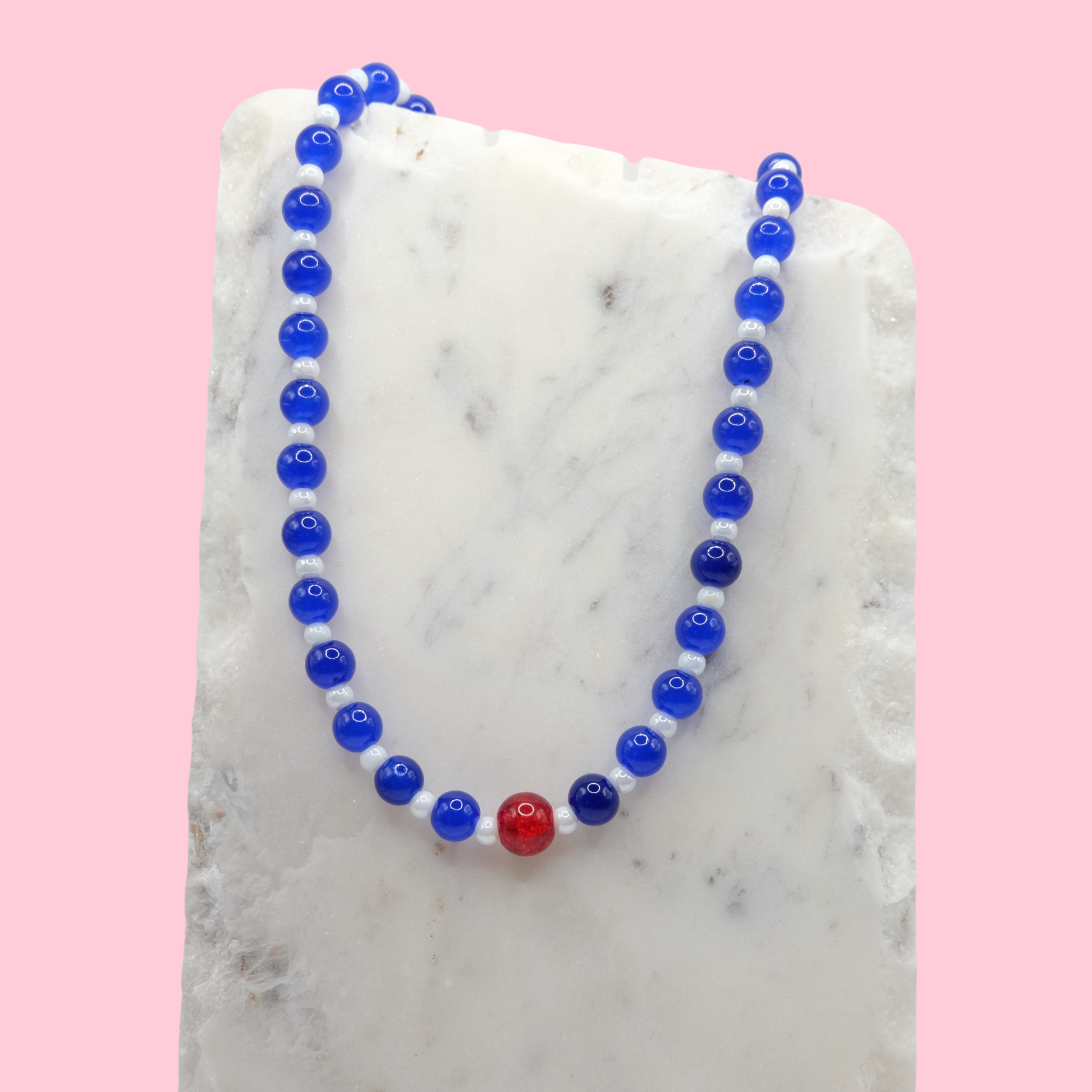 Necklace with blue and red glass beads on a marble surface with a pink background