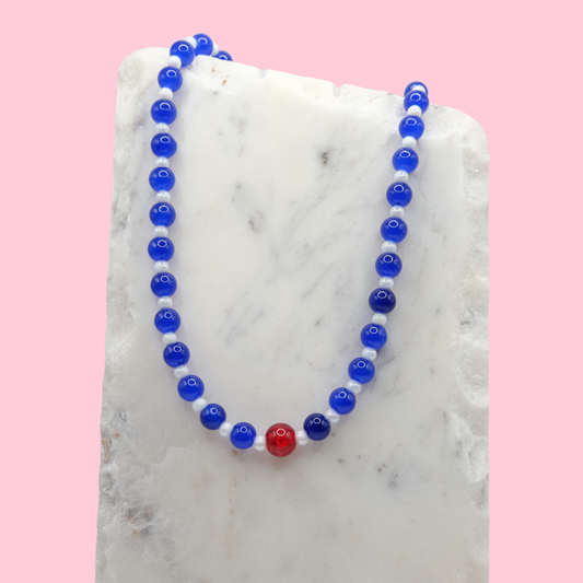 Necklace with blue and red glass beads on a marble surface with a pink background