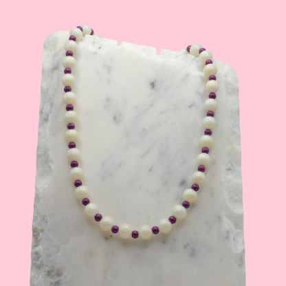 Pearl necklace with purple accents on a marble surface with a pink background