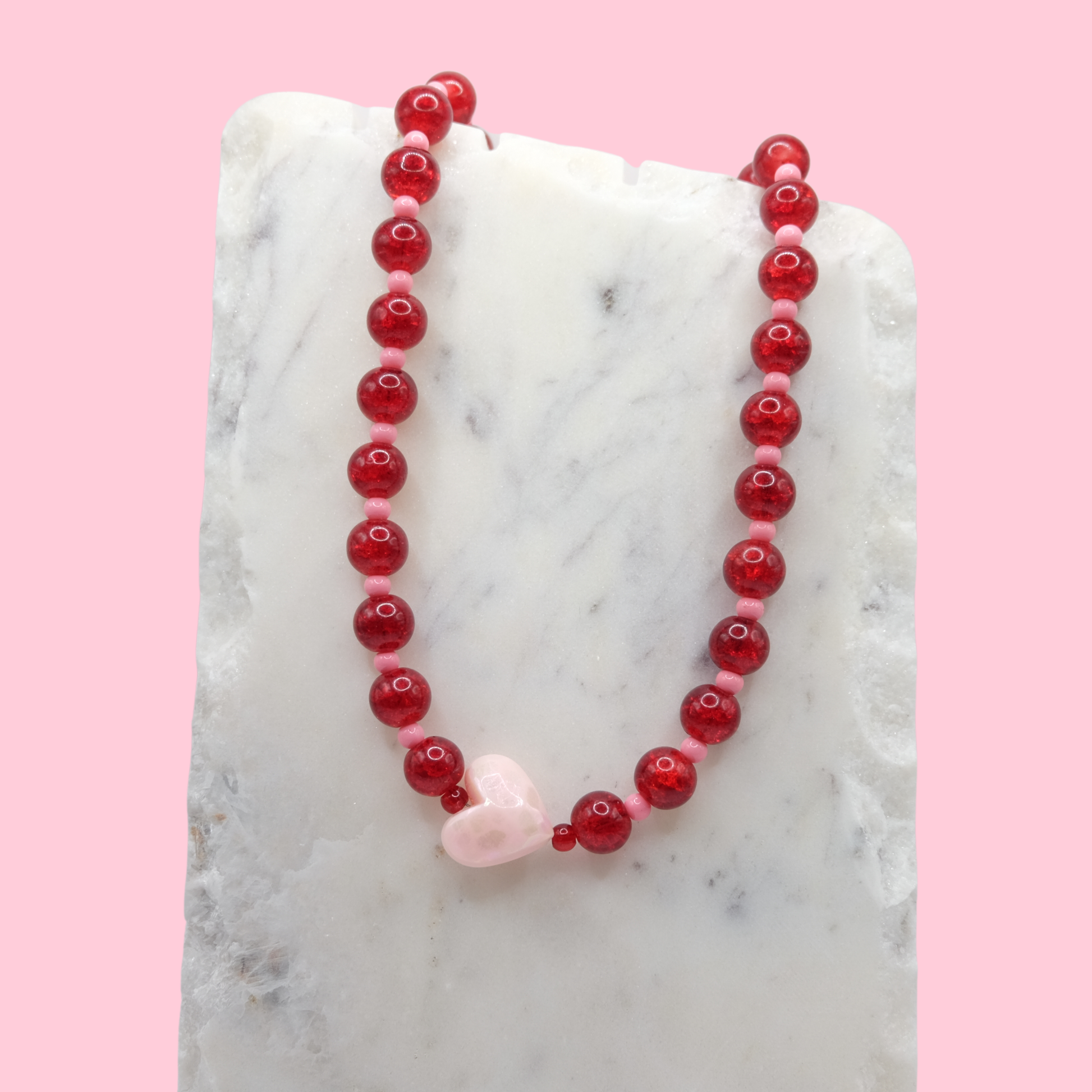Beaded necklace with red and pink beads on a marble surface with a pink background