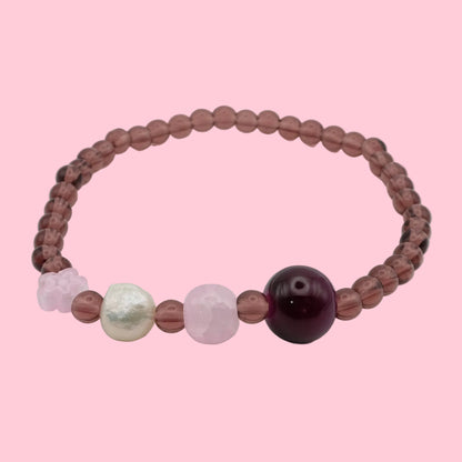An elastic beaded bracelet composed of light burgundy 4mm glass beads, featuring a plum glass bead, soft pink glass bead, freshwater pearl, and translucent pink flower bead, shown on a white background.