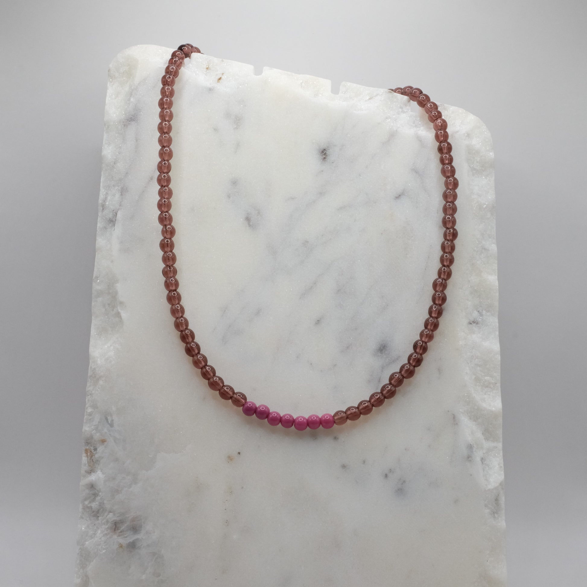 Beaded necklace with alternating red and pink beads on a marble surface