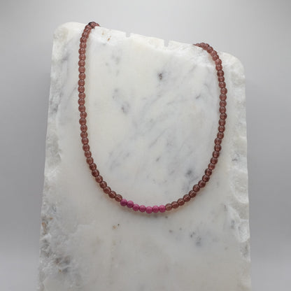Beaded necklace with alternating red and pink beads on a marble surface