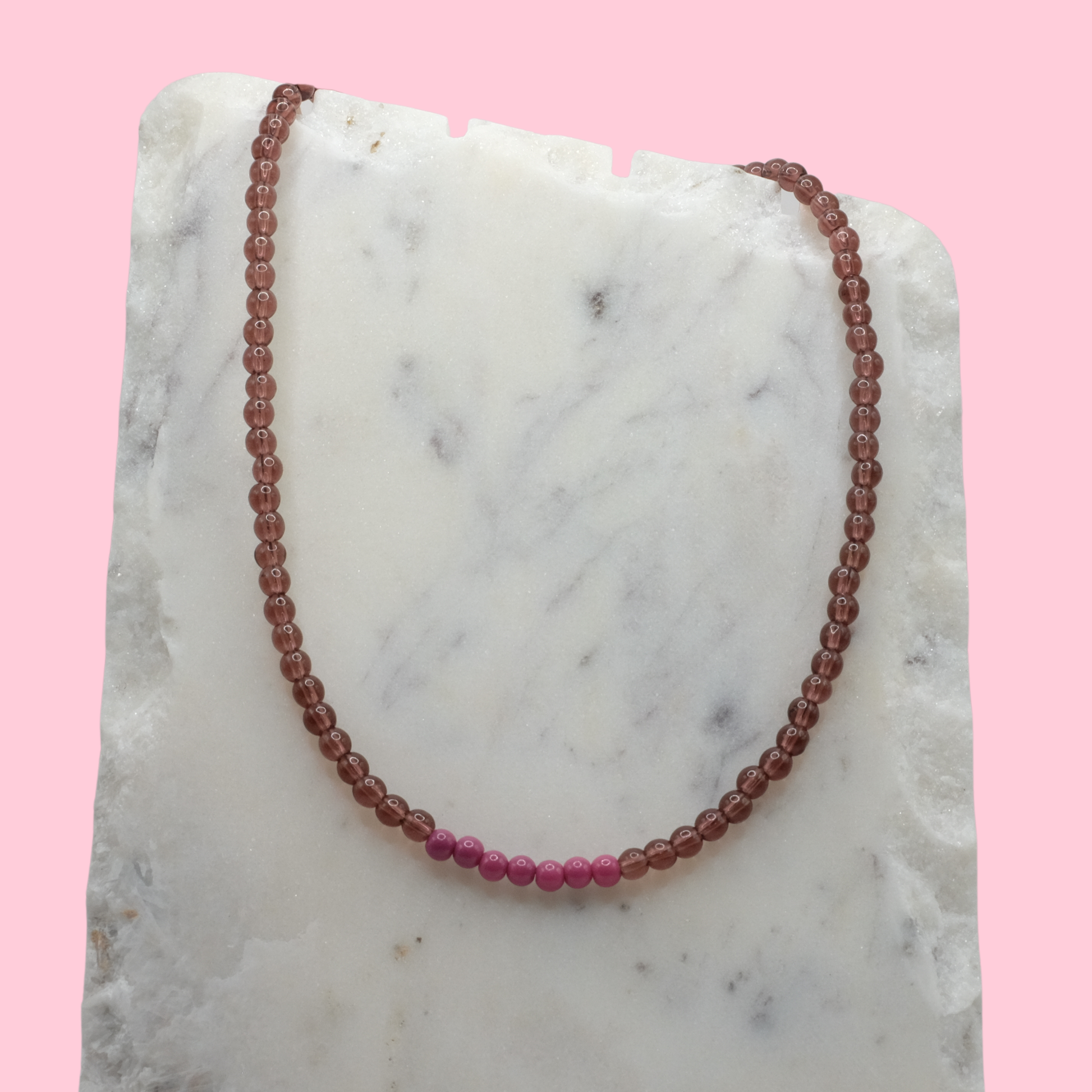 Necklace with alternating red and pink beads on a marble surface with a pink background