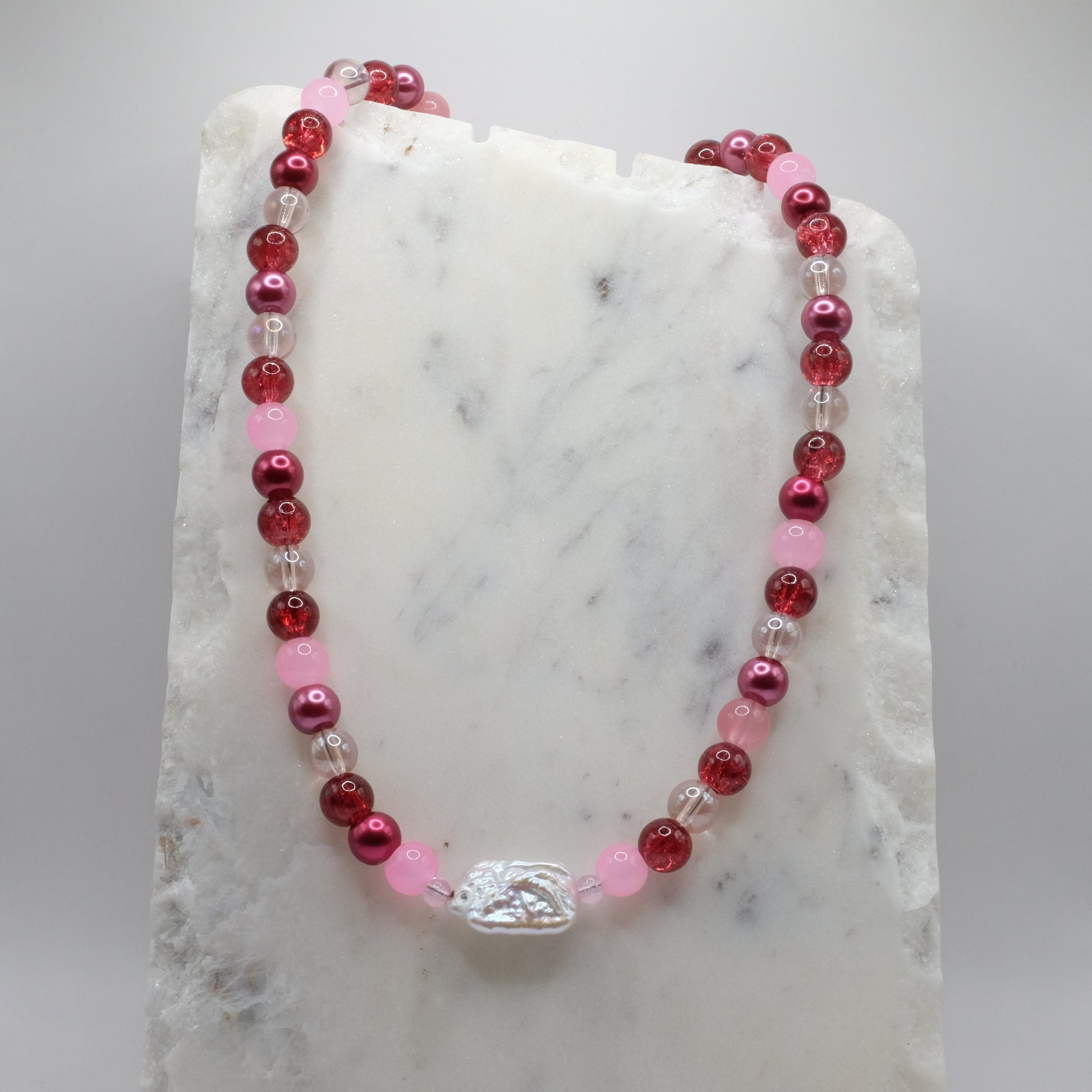 Beaded necklace with red, pink, and clear beads on a marble surface