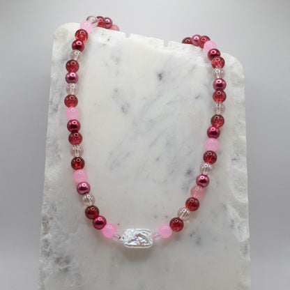 Beaded necklace with red, pink, and clear beads on a marble surface