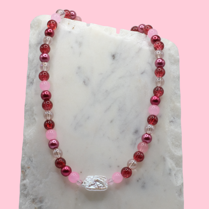 Beaded necklace with red, pink, and clear beads on a marble surface with a pink background
