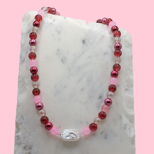Beaded necklace with red, pink, and clear beads on a marble surface with a pink background