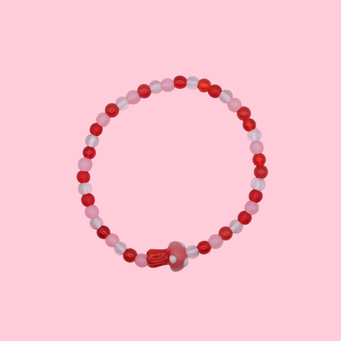 An elastic beaded bracelet made with 4mm glass beads in  red and pink tones, featuring a pink and red blown glass toadstool bead, shown on a white background.