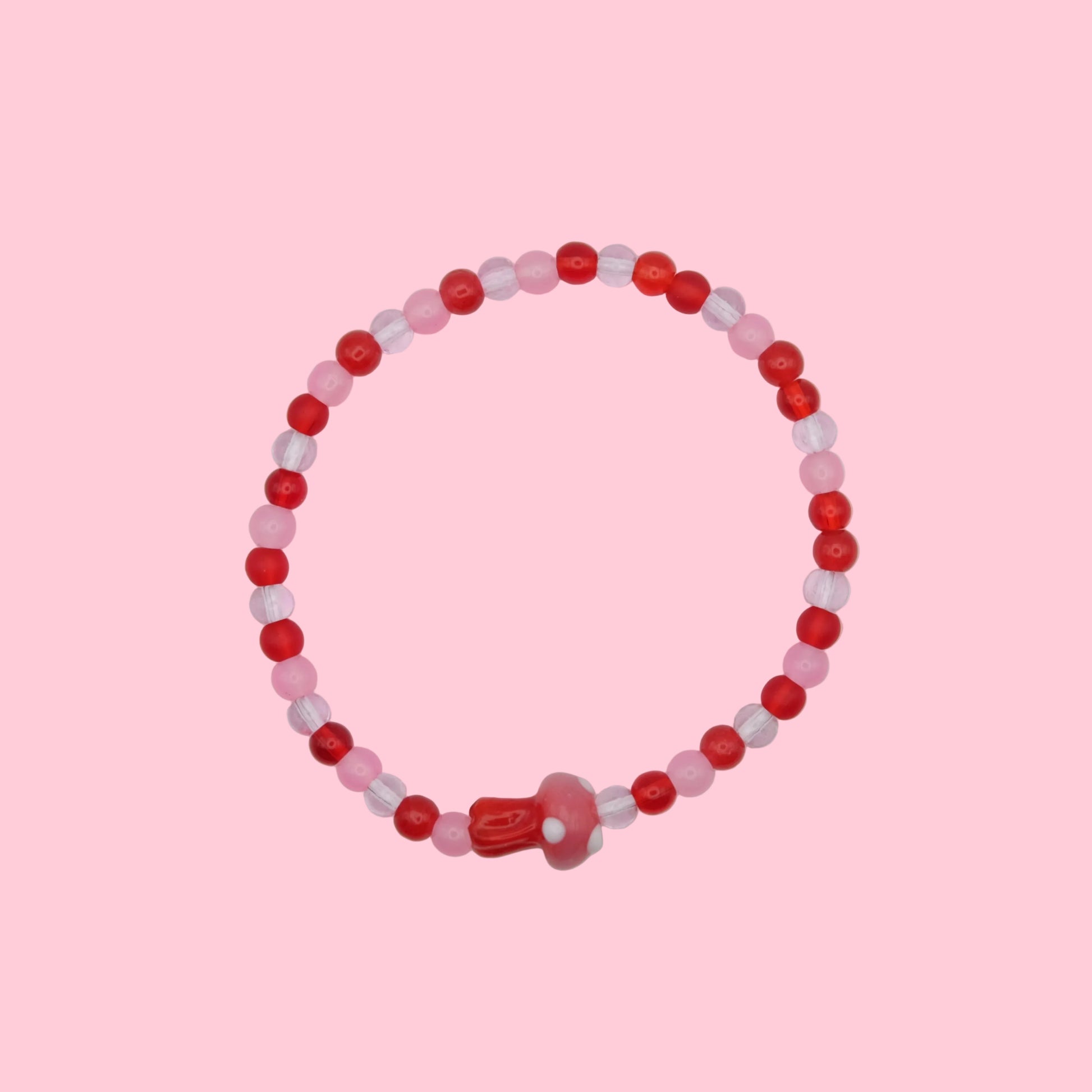 An elastic beaded bracelet made with 4mm glass beads in  red and pink tones, featuring a pink and red blown glass toadstool bead, shown on a white background.