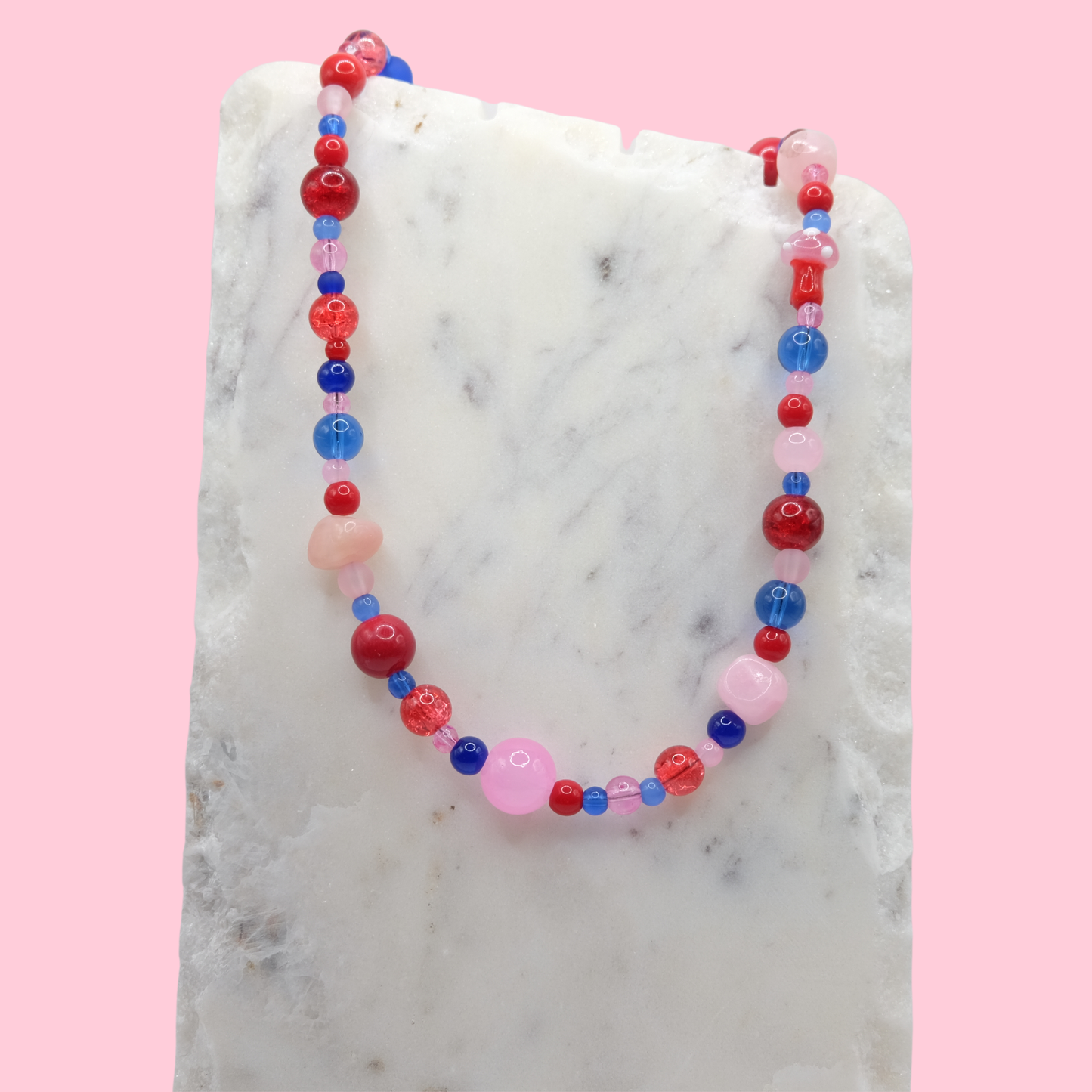 Colorful beaded necklace on a marble surface with a pink background