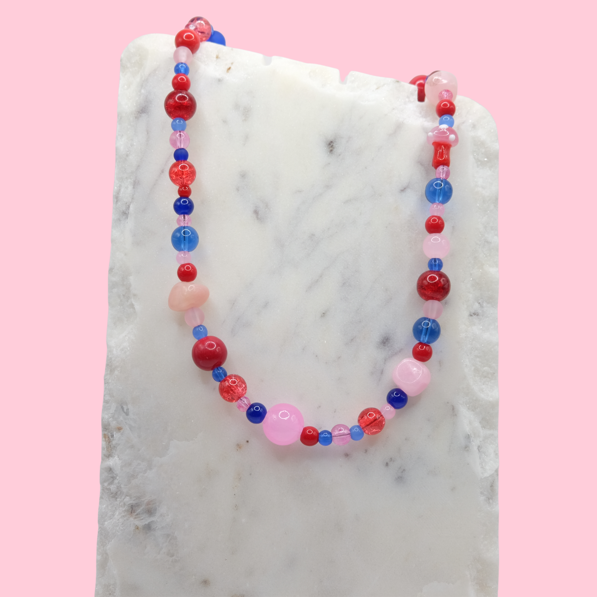 Colorful beaded necklace on a marble surface with a pink background