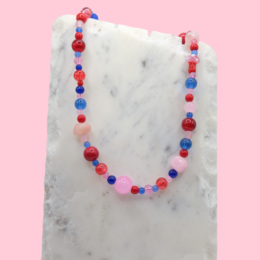 Colorful beaded necklace on a marble surface with a pink background