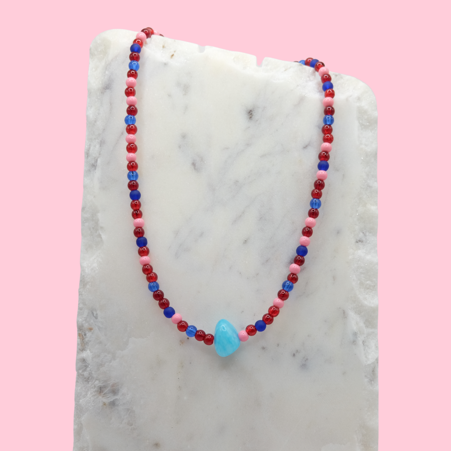 Beaded necklace with red, blue, and pink beads on a marble surface with a pink background