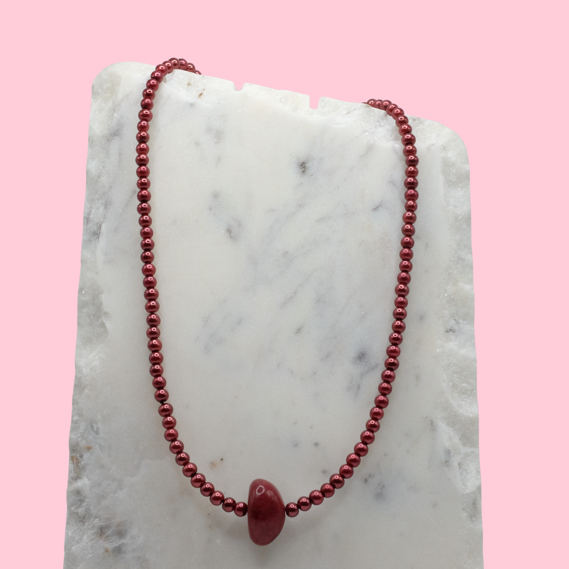 Red beaded necklace on a marble surface with a pink background