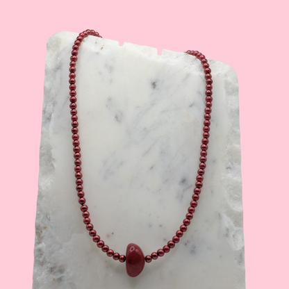 Red beaded necklace on a marble surface with a pink background