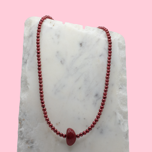 Red beaded necklace on a marble surface with a pink background