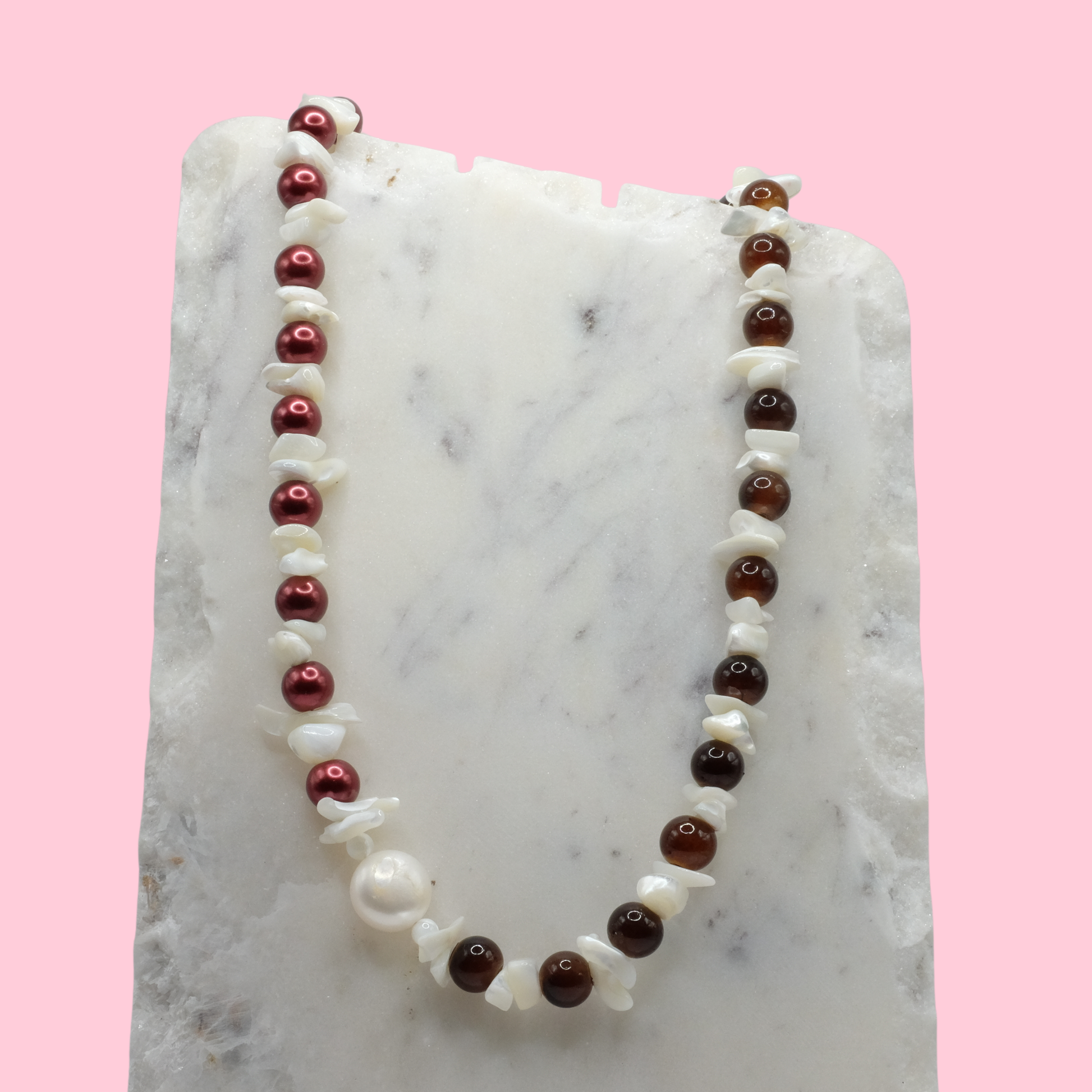 Necklace with red, white, and brown beads on a marble surface with a pink background