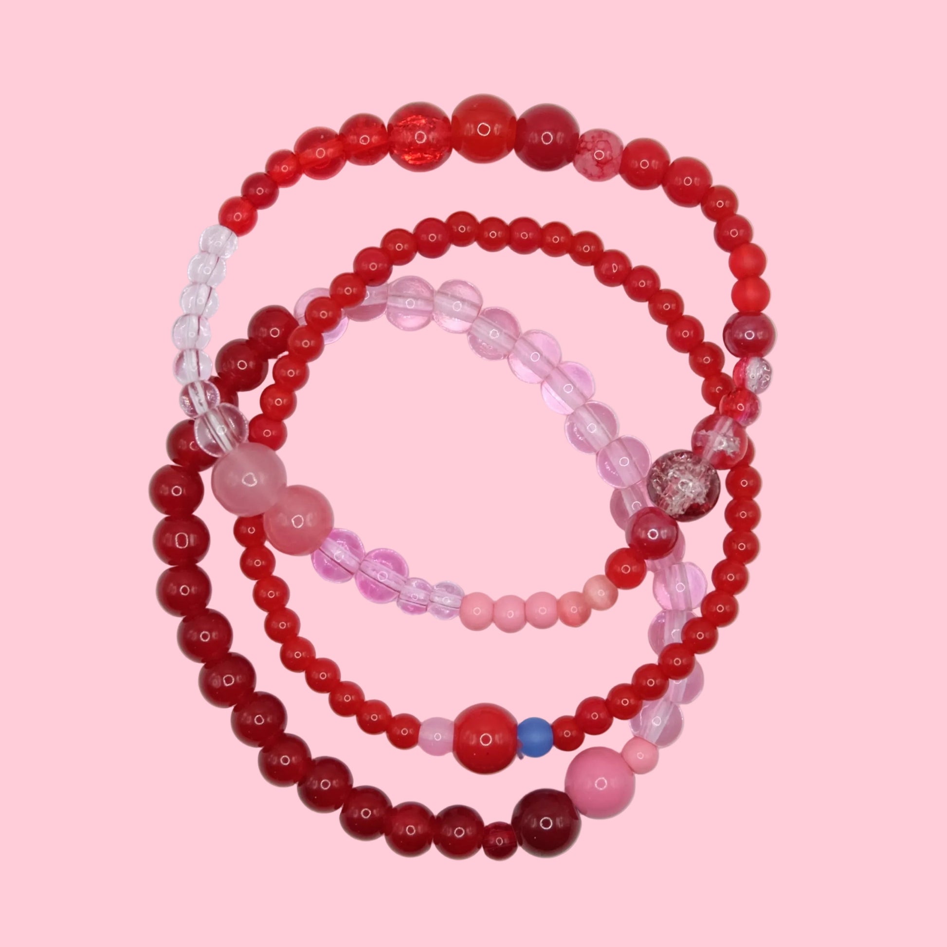 A handmade elastic bracelet stack featuring mixed glass beads in bright pink, deep red and blue tones with varied bead sizes.