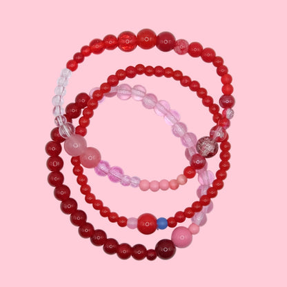 A handmade elastic bracelet stack featuring mixed glass beads in bright pink, deep red and blue tones with varied bead sizes.