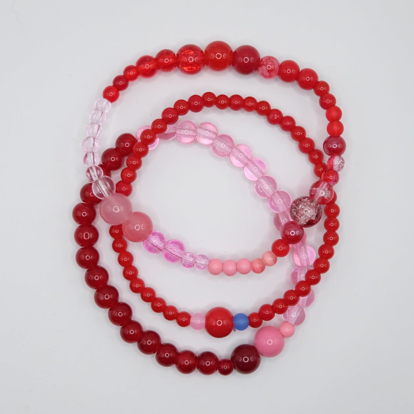 A stack of 3 beaded bracelets, in red and pink on a light gray background.