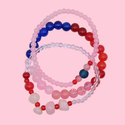 A one of a kind elastic beaded bracelet stack composed of mixed 4mm to 8mm glass beads in pink, red and blue tones, shown on a neutral background.