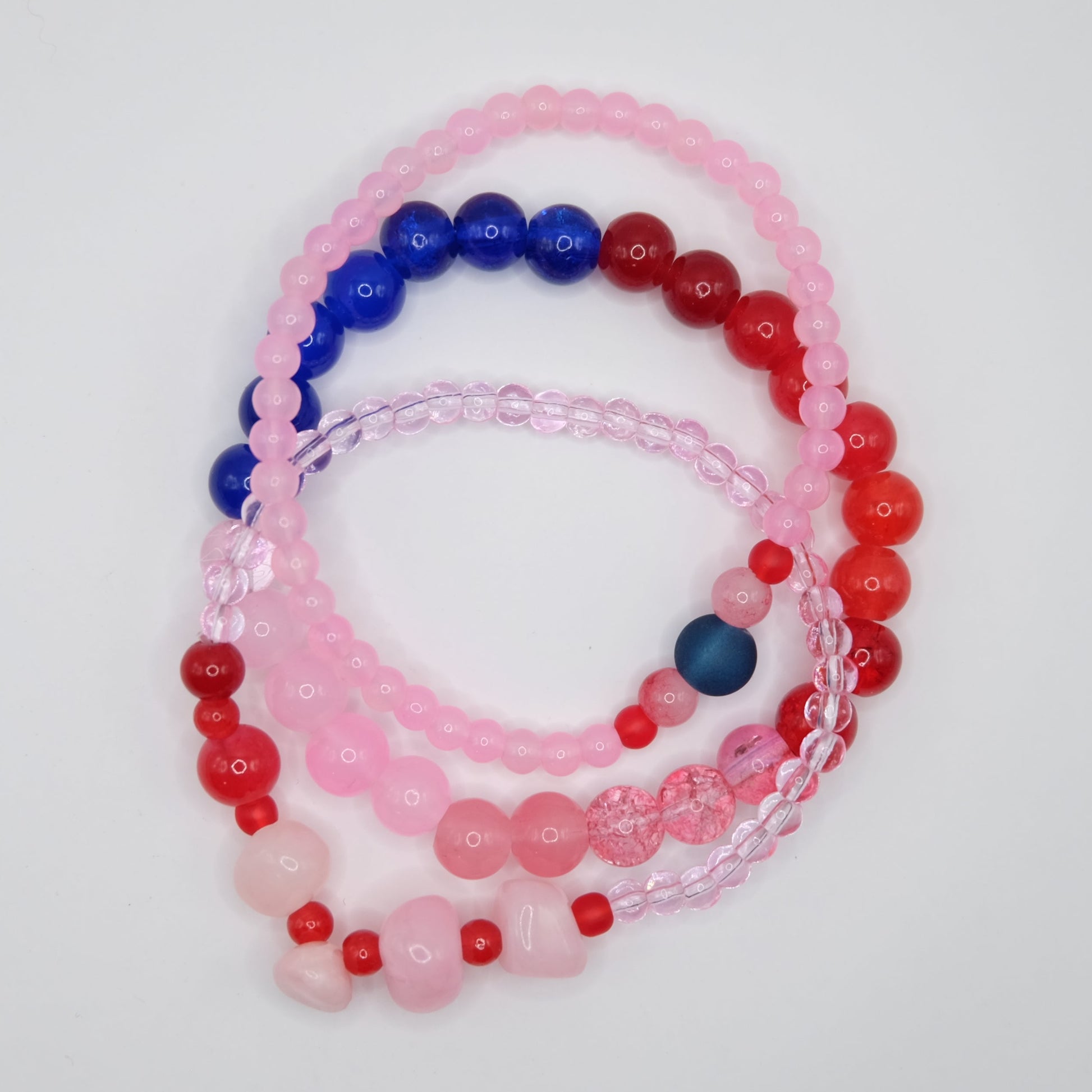 Set of beaded bracelets in pink, blue, and red on a light gray background