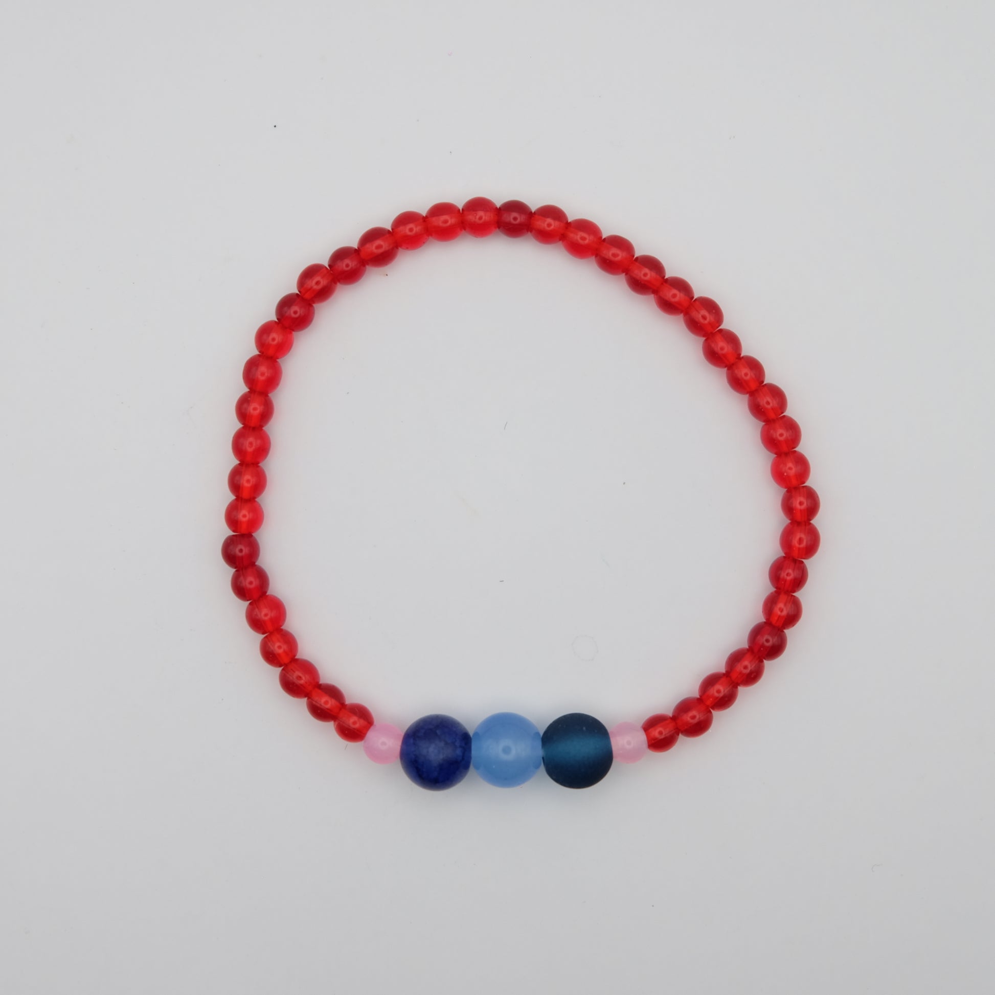 A single red beaded bracelet with a an accent of 3 large blue beads and 2 smaller pink beads on either side on a plain background .