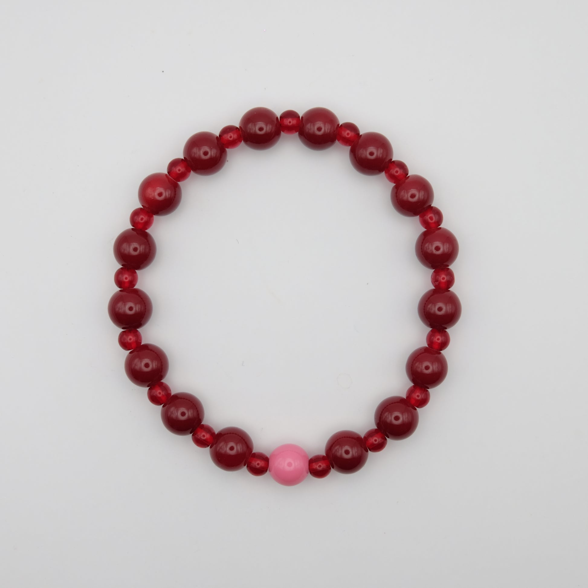 Beaded bracelet with red and pink beads on a plain background