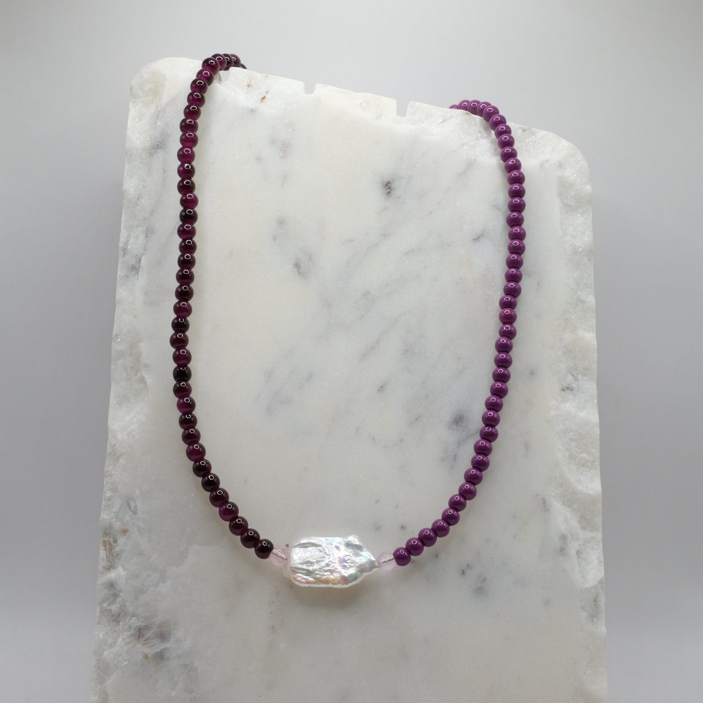 Beaded necklace with a large central crystal on a marble surface